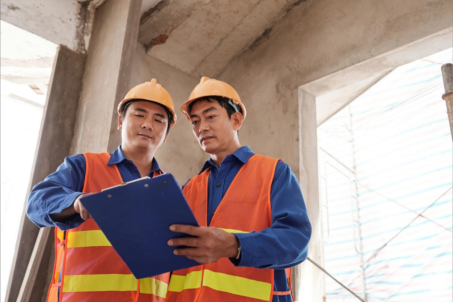 Two contractors in orange vests checking a report on a clipboard.