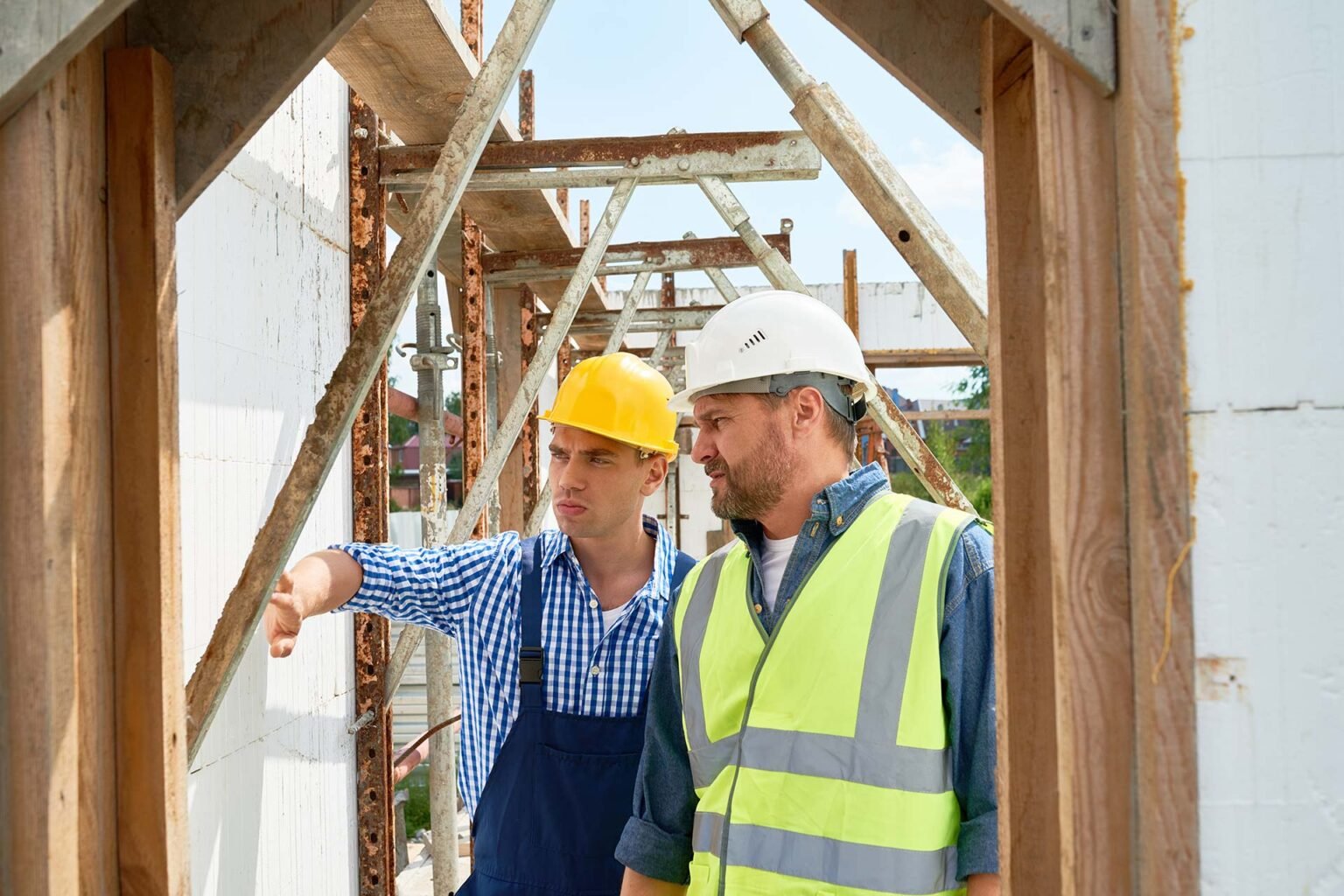 Two builders discussing work beneath scaffolding.