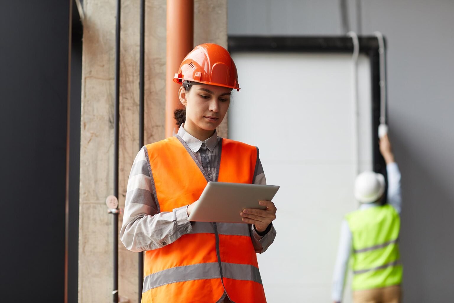 A site supervisor in an orange hard hat checking quantities on a tablet.